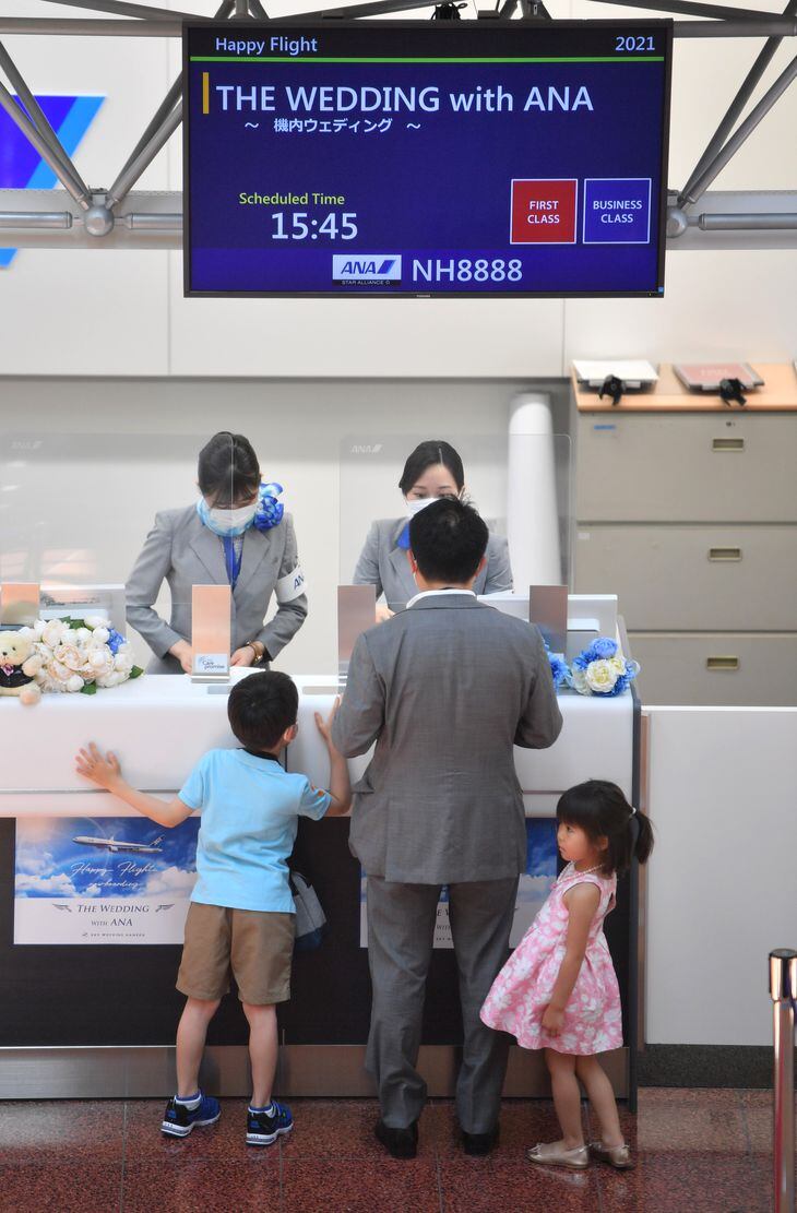 通常は国際線の搭乗手続きをするチェックインカウンターで、受付をおこなう結婚式の参列者。搭乗案内の掲示板も挙式仕様になっている =羽田空港